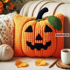 a crocheted pumpkin pillow sitting on top of a couch next to a cup of coffee