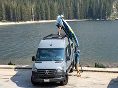 two people standing on top of a van with surfboards