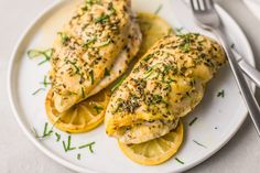 two pieces of chicken on a plate with lemon slices