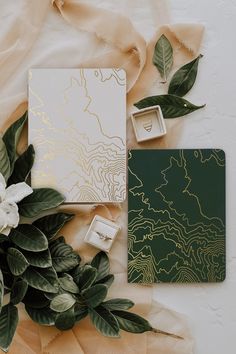 the wedding stationery is surrounded by greenery and gold leafy paper accents, which are on display