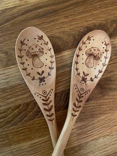 two wooden spoons with designs on them sitting on top of a wood table next to each other