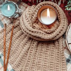 a knitted scarf with a lit candle and two tea lights on it next to other items