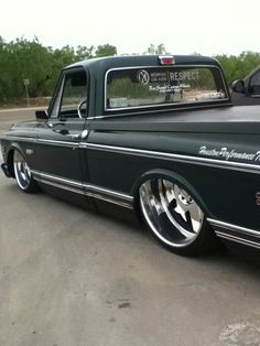 an old black pickup truck with chrome rims parked in a parking lot next to another car