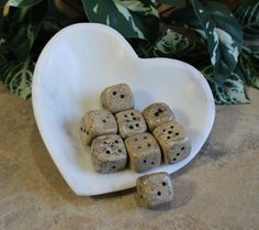 a heart shaped bowl filled with dices sitting on top of a table next to a potted plant