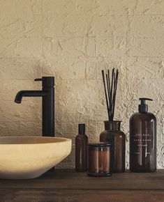 a bathroom sink with soap dispenser, reeds and bottles next to it