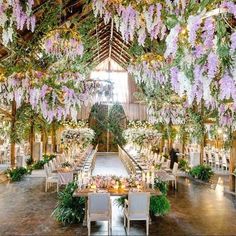 an indoor wedding venue with purple flowers hanging from the ceiling