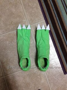 the legs of someone wearing green slippers with white spikes on them, standing next to a rug