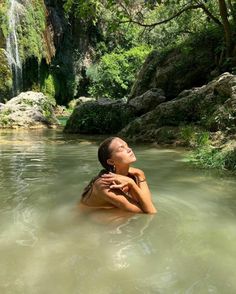 a woman in the water with her arms around her neck looking up at a waterfall