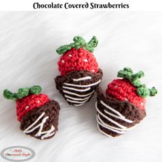 three crocheted strawberries are sitting on a white furnishing area, one is brown and the other is red