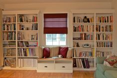 a living room filled with lots of books on top of white bookcases next to a window