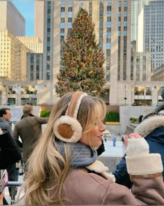 a woman wearing ear muffs standing in front of a christmas tree