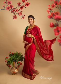 a woman in a red sari standing next to a tree with flowers on it