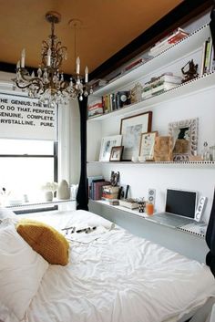 a white bed sitting under a chandelier in a bedroom next to a window