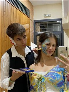 two people with face paint on their faces taking a selfie in front of a mirror