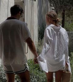 the man and woman are walking down the street holding hands, both wearing white shirts