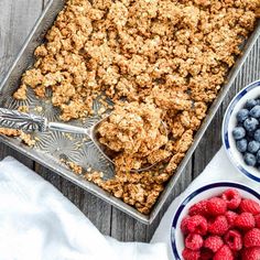 a pan filled with granola next to bowls of berries and blueberries