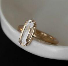 two gold rings with an oval cut diamond on top, sitting in front of a white bowl