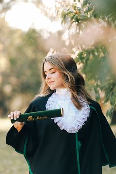 a woman in a black robe holding a green bat and wearing a white collared shirt