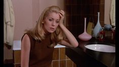 a woman sitting in front of a bathroom sink with her hand on her head and looking at the camera