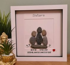 two pebbles are placed in a white frame on a table next to a potted plant