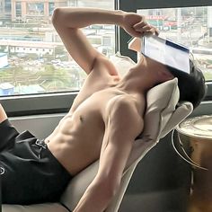 a shirtless man laying on top of a couch next to a window with cityscape in the background