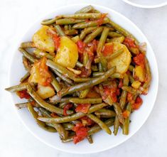 a white plate topped with green beans covered in tomato sauce and sliced potatoes on the side