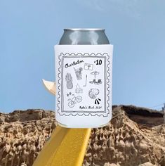 a can of beer sitting on top of a yellow pole next to some rocks and a blue sky