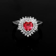 a heart shaped ruby and diamond ring on a black surface with white diamonds surrounding it