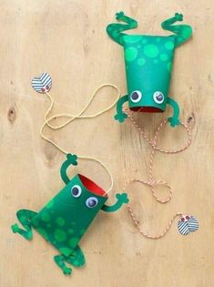 two green paper hats with eyes and legs hanging from strings on a wooden table top