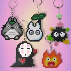 four pixel keychains are hanging on a pink background, each with different characters