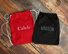 two personalized drawstring bags sitting on top of a wooden floor next to each other