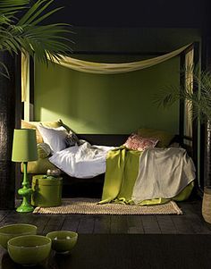 a bedroom with green walls and white bed linens on the bottom, along with palm trees in the background