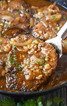 meat and onions are being cooked in a skillet with a spoon on the side