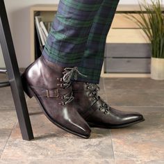 a man in plaid pants and black boots is standing on a chair with his legs crossed