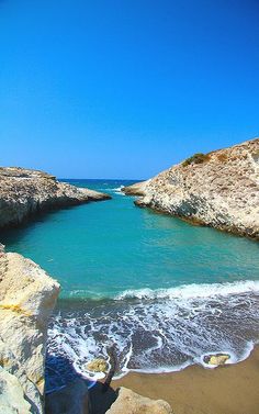 the water is crystal blue and clear at this beach near some rocky cliffs, with waves coming in from the shore