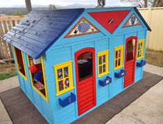 a blue and red play house with lots of windows on the front door, sitting on top of a wooden mat