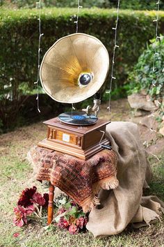 an old fashioned record player sitting on top of a blanket in the grass next to flowers