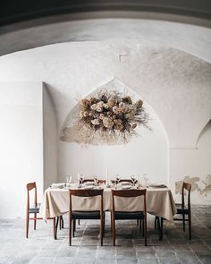 a dining room table set for four with flowers hanging from the ceiling