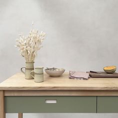 a wooden table topped with two vases filled with white flowers next to a bowl