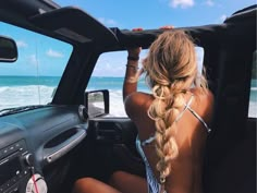 a woman sitting in the driver's seat of a car looking out at the ocean