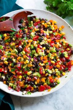 a white bowl filled with black beans, corn and avocado salad next to a wooden spoon