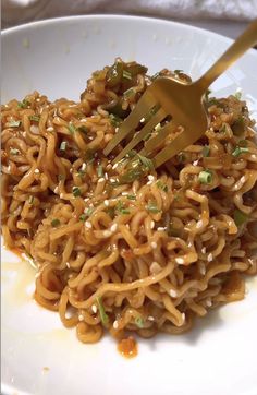 a white plate topped with noodles covered in sesame seeds and green onions next to a fork