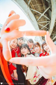 a group of young women standing next to each other in front of a bridge holding up a hand