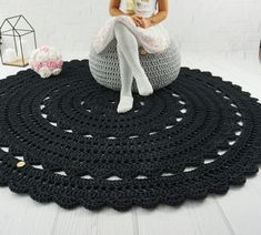 a woman sitting on top of a black crocheted rug