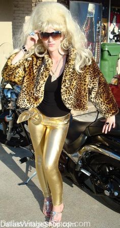 a woman in gold pants and leopard print jacket posing for the camera on her motorcycle