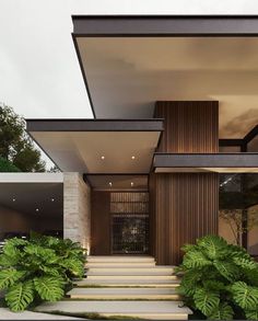 a modern house with stairs leading up to the front door and green plants growing on the side