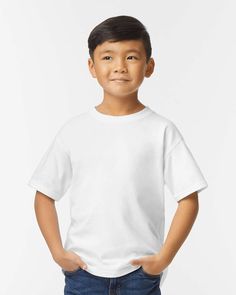 a young boy wearing a white t - shirt with his hands in his pockets and smiling at the camera