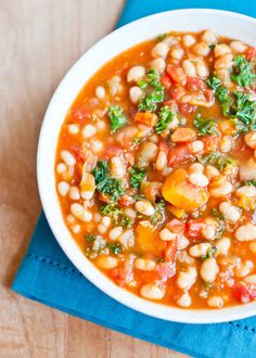 a white bowl filled with beans and spinach on top of a blue napkin next to a wooden table