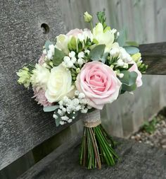 a bridal bouquet sitting on top of a wooden bench in front of a fence