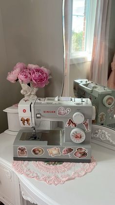 a sewing machine sitting on top of a white table next to a vase with pink flowers